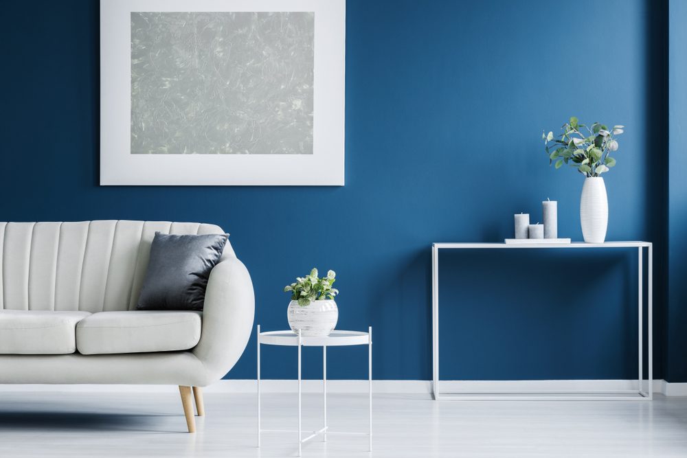 Metal console table with plant in vase and candles standing against blue wall in living room